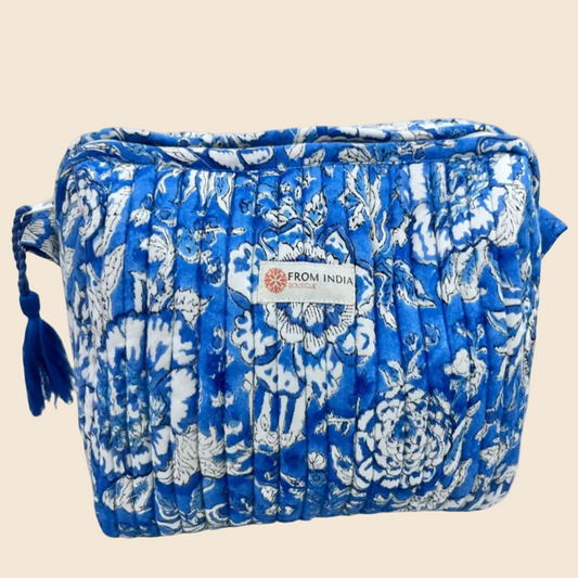 Trousse de toilette matelassée bleue From India Boutique, en coton imprimé floral artisanal, avec fermeture zippée et pompon bleu, présentée sur fond beige.