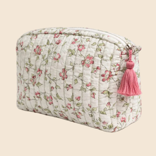 Trousse de toilette matelassée blanche From India Boutique, en coton imprimé floral artisanal rose, vert et taupe, avec étiquette cousue et pompon rose, présentée sur fond beige.