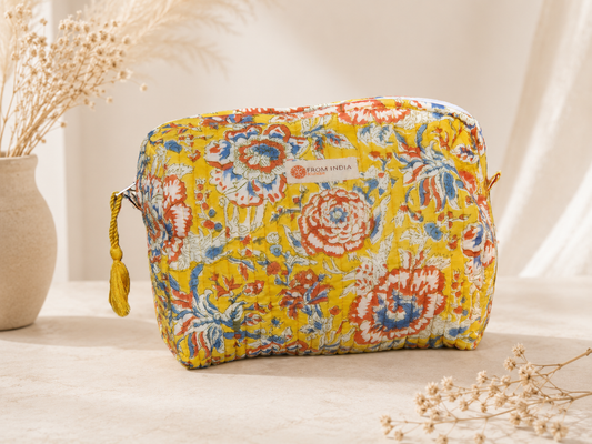 Trousse de toilette matelassée jaune From India Boutique, en coton imprimé floral artisanal rouge, bleu et blanc, avec fermeture zippée et pompon jaune, présentée dans une ambiance bohème lumineuse