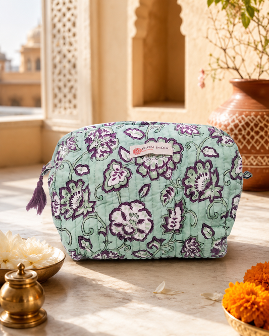 Trousse de toilette matelassée vert d’eau From India Boutique, en coton imprimé floral violet et blanc, présentée dans une ambiance lumineuse inspirée de l’Inde avec décor artisanal et fleurs.
